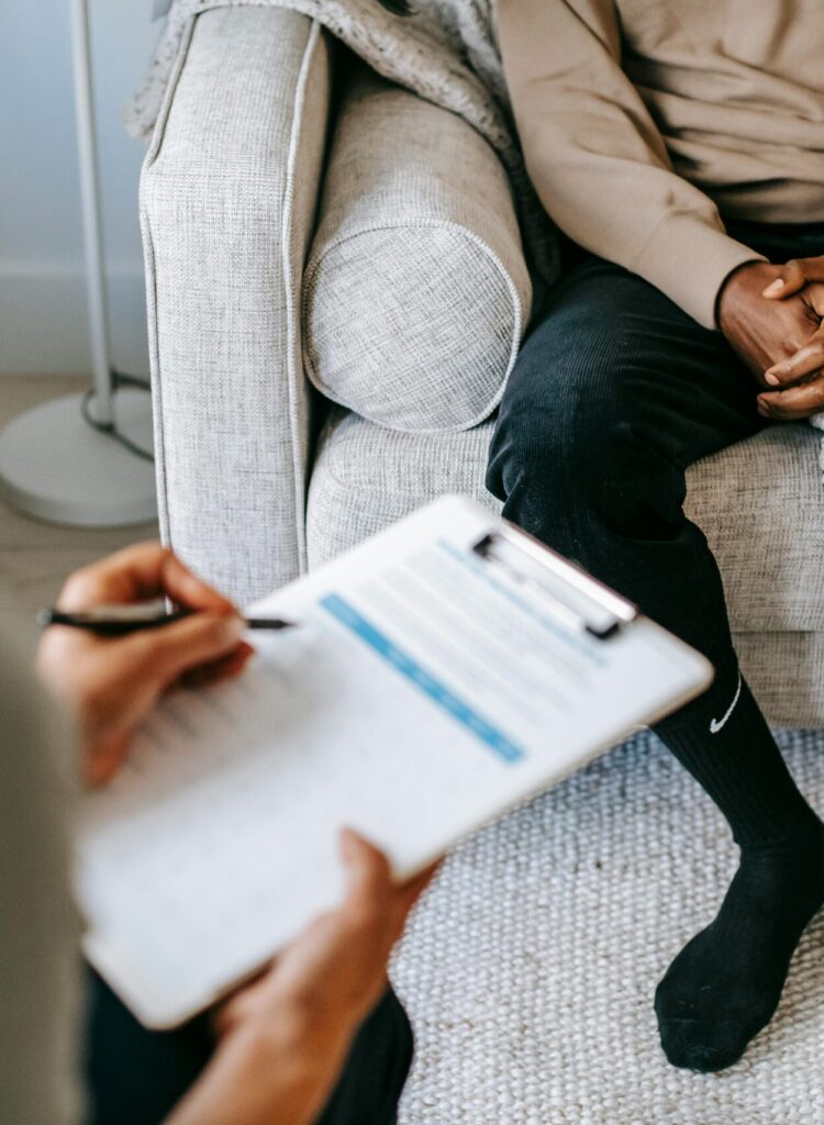 Therapist takes notes as client sits on a sofa during a psychotherapy session.