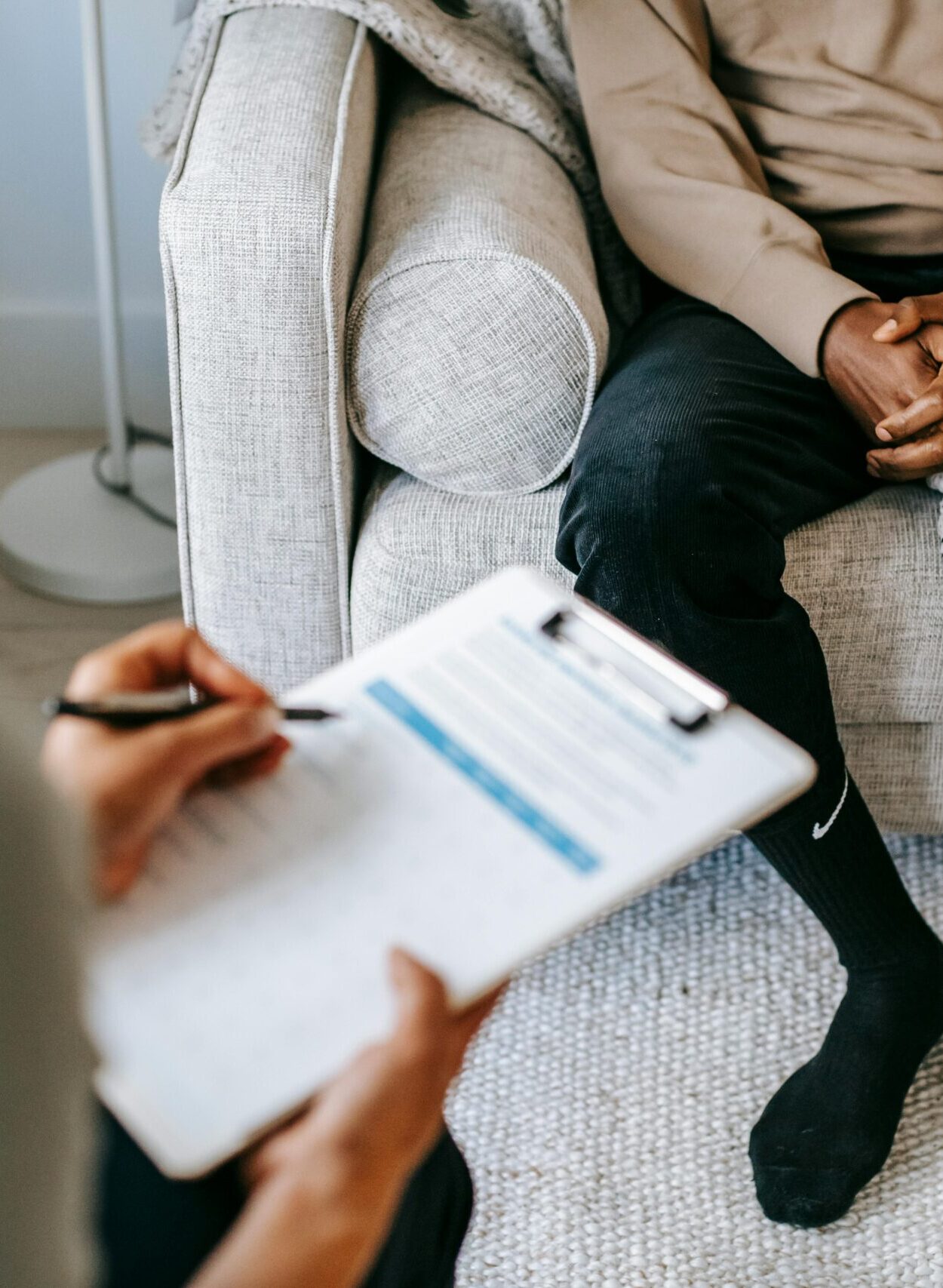 Therapist takes notes as client sits on a sofa during a psychotherapy session.